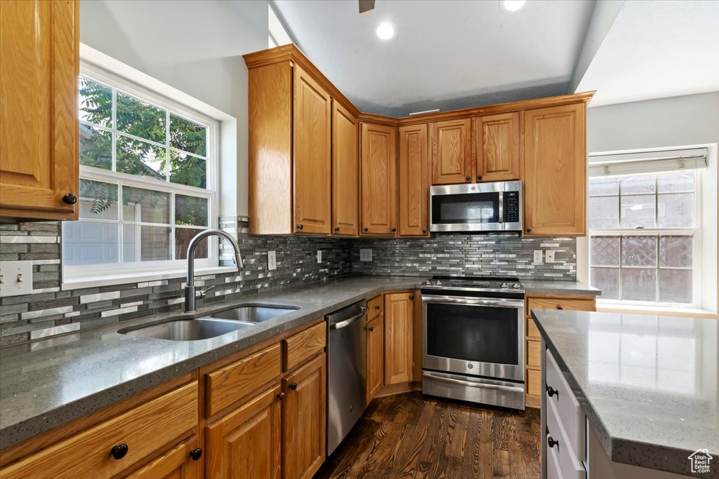 Kitchen featuring stainless steel appliances, dark stone countertops, dark wood-type flooring, and brown cabinets