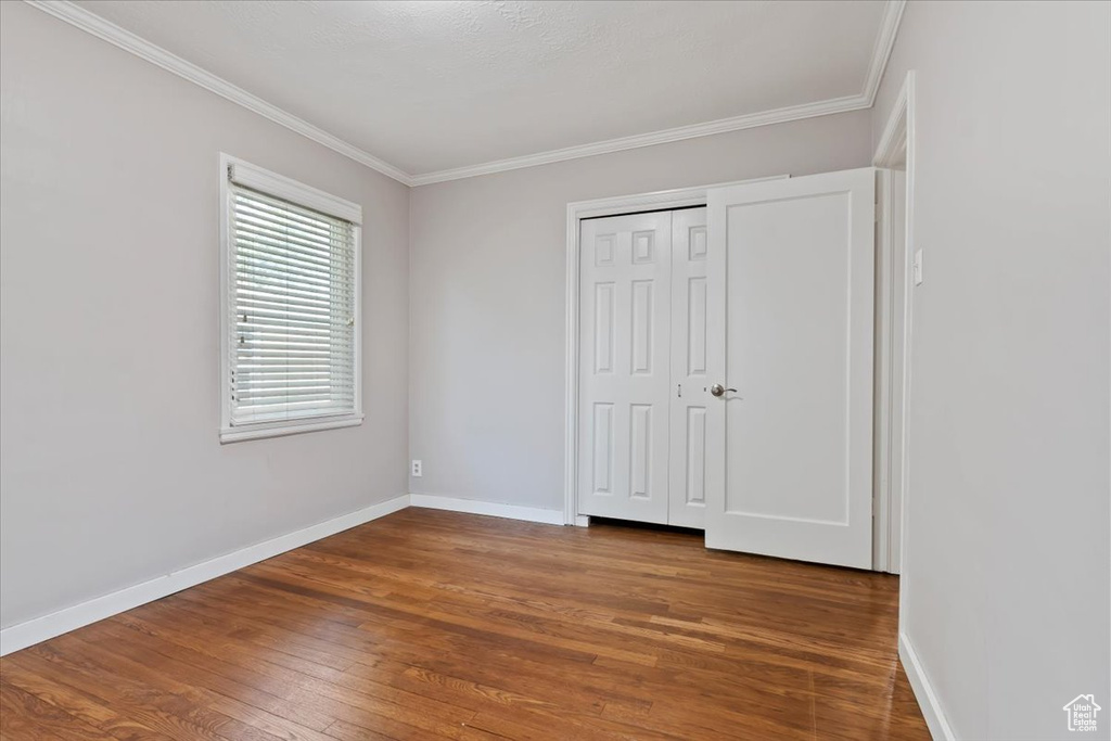 Unfurnished bedroom with wood finished floors, ornamental molding, and a closet