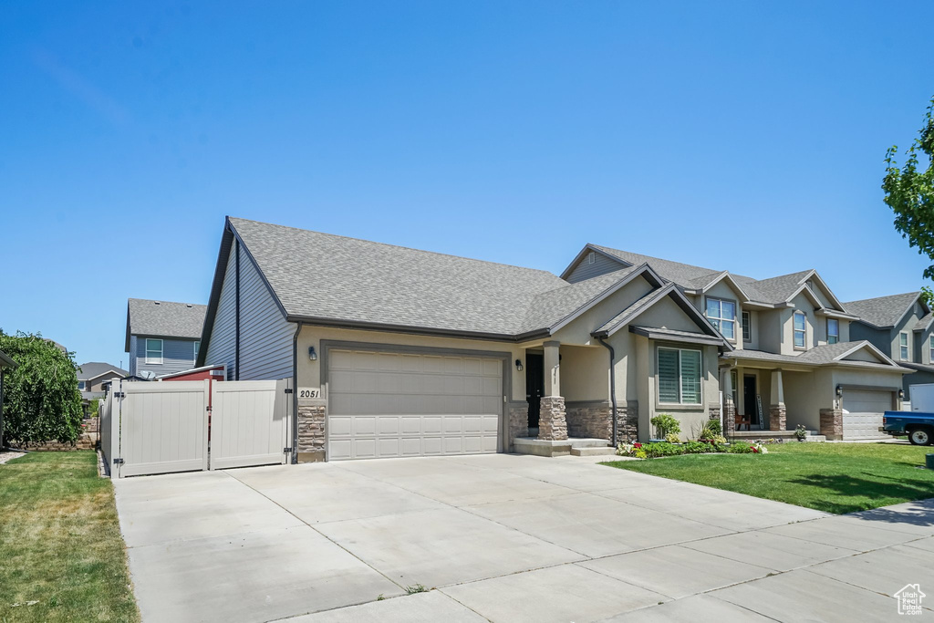 View of front facade featuring a garage, driveway, stone siding, and roof with shingles