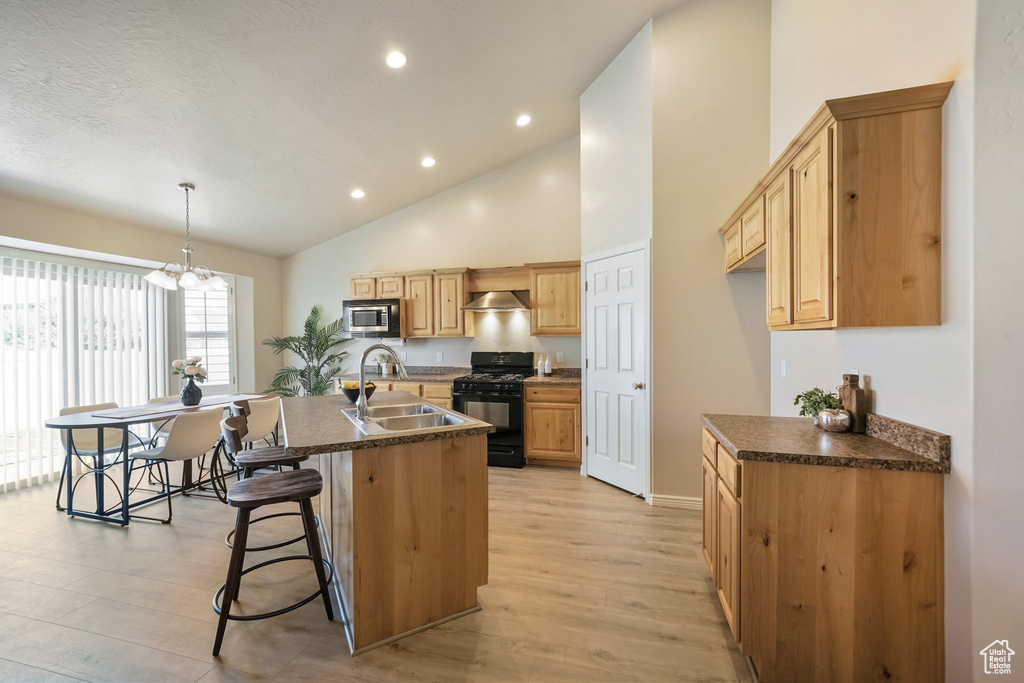 Kitchen with black gas stove, stainless steel microwave, dark countertops, light wood finished floors, and high vaulted ceiling
