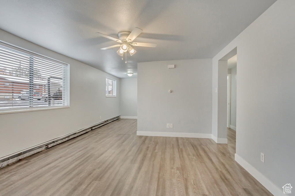 Empty room with a ceiling fan, light wood-style flooring, baseboards, and baseboard heating
