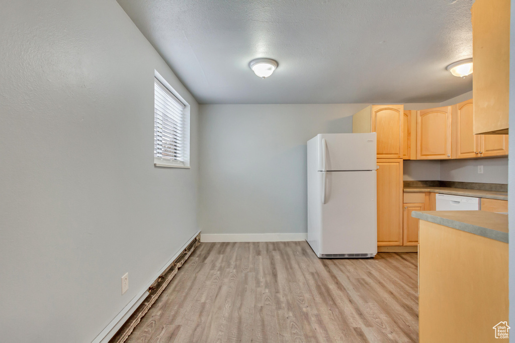 Kitchen with white appliances, light brown cabinets, light wood finished floors, and baseboards