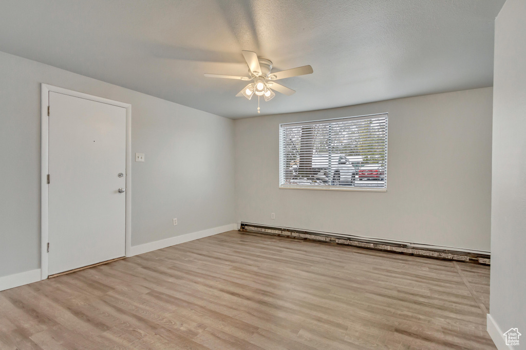 Empty room featuring ceiling fan, wood finished floors, baseboards, and baseboard heating