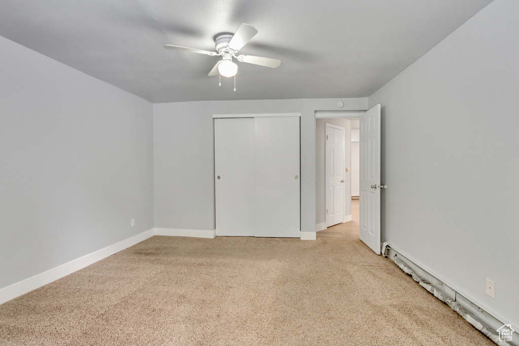 Unfurnished bedroom with light colored carpet, baseboard heating, a closet, baseboards, and a ceiling fan