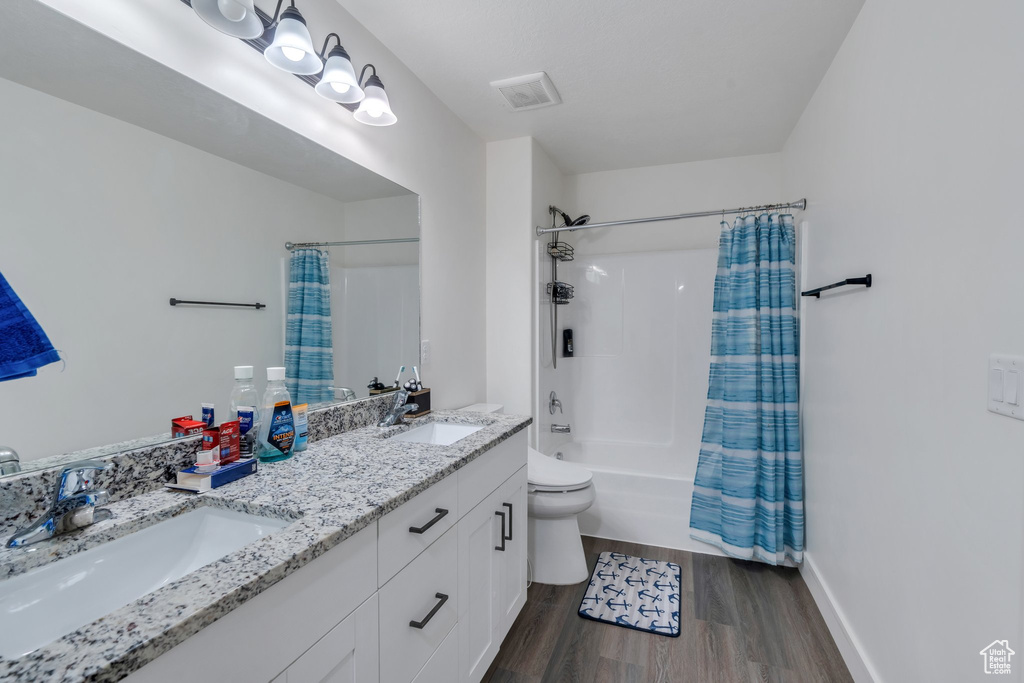 Bathroom with wood finished floors, shower / bath combination with curtain, and double vanity