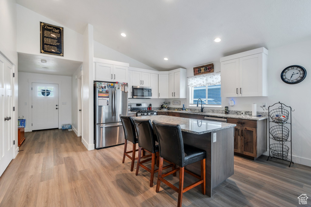 Kitchen with appliances with stainless steel finishes, vaulted ceiling, a breakfast bar area, light stone counters, and white cabinets