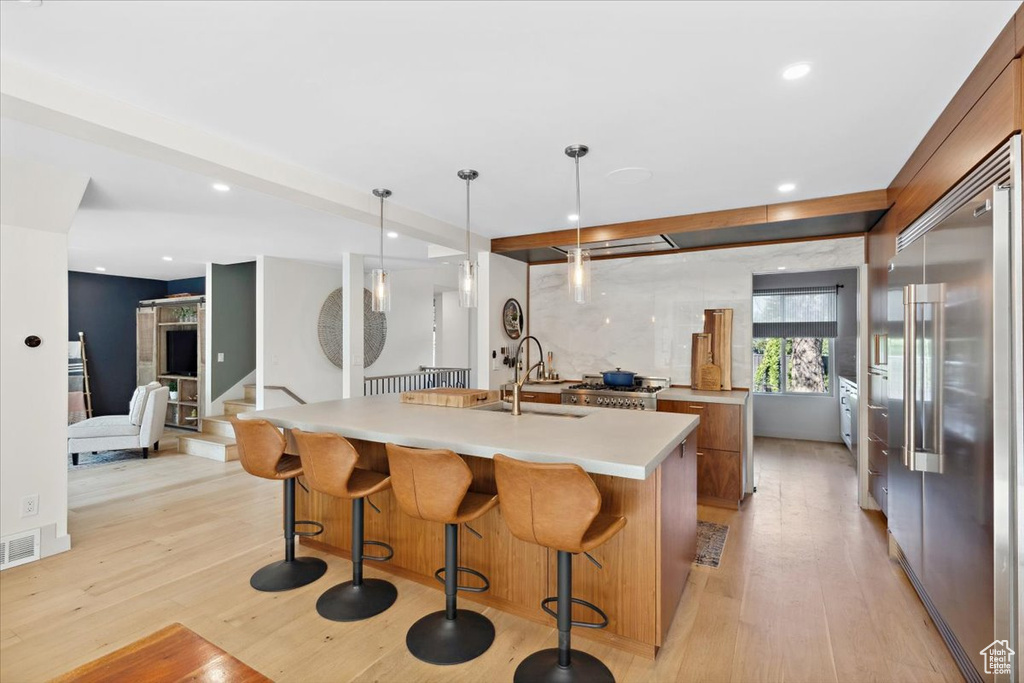 Kitchen featuring built in fridge, light wood-type flooring, light countertops, recessed lighting, and a kitchen island with sink