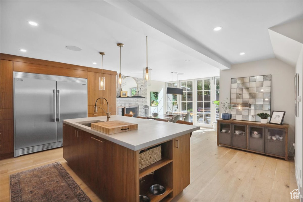 Kitchen featuring stainless steel built in refrigerator, modern cabinets, light wood-type flooring, a brick fireplace, and recessed lighting
