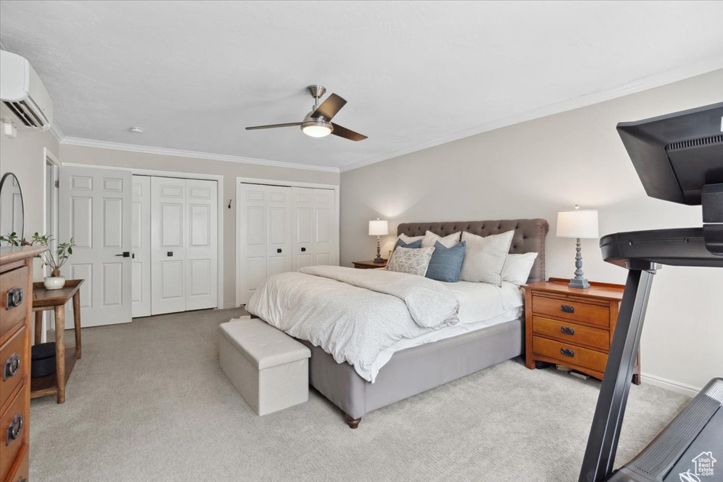 Carpeted bedroom featuring an AC wall unit, multiple closets, ornamental molding, and ceiling fan