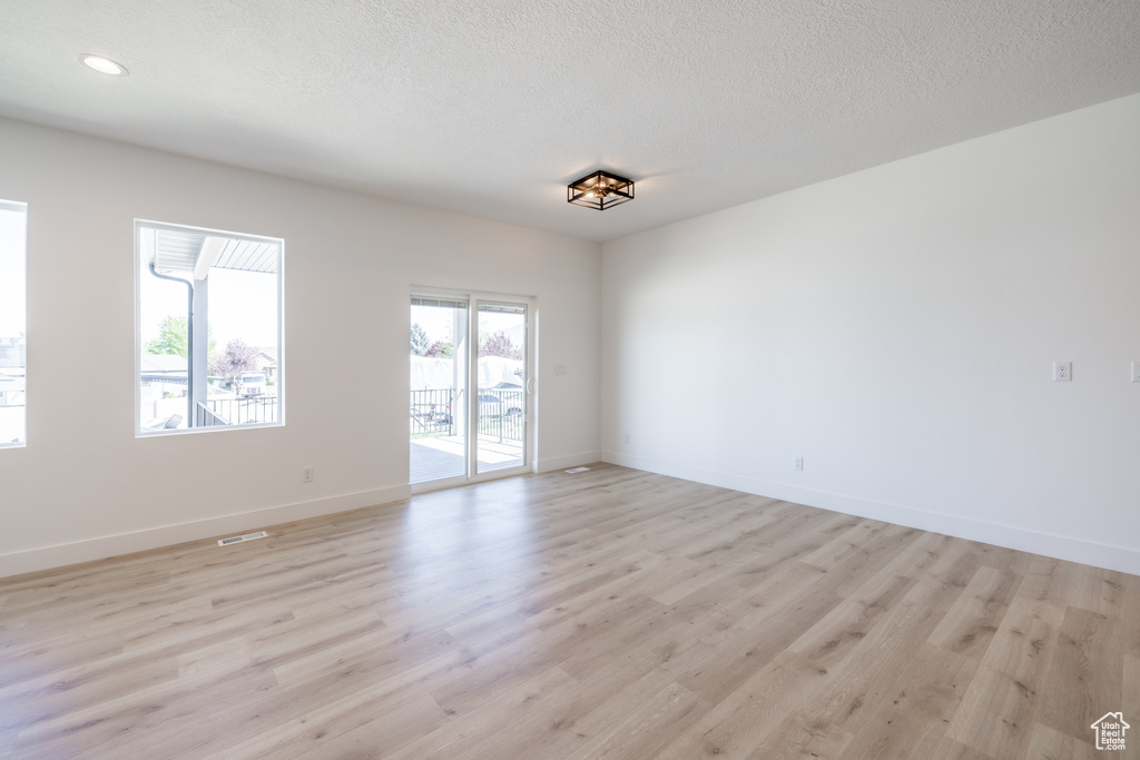 Empty room with light wood-type flooring, a textured ceiling, and recessed lighting