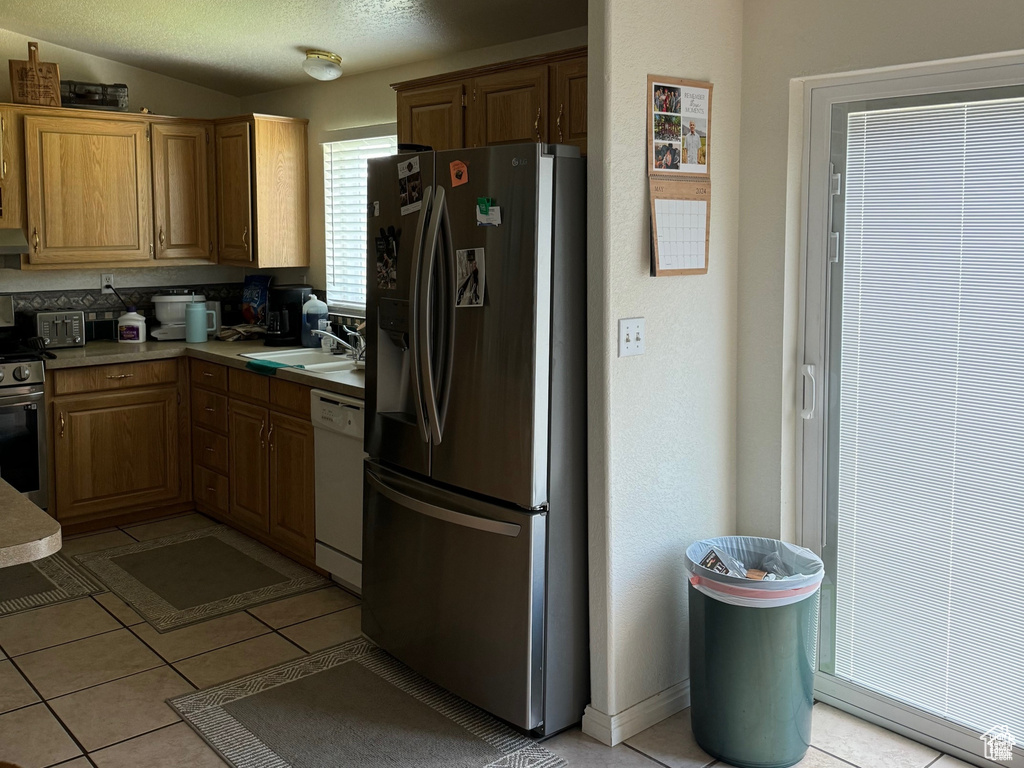 Kitchen featuring stainless steel appliances, light countertops, light tile patterned flooring, under cabinet range hood, and vaulted ceiling