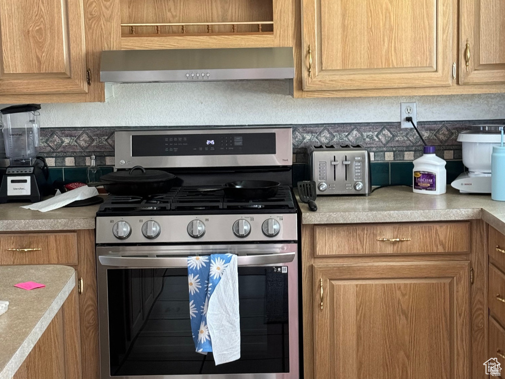 Kitchen featuring stainless steel range with gas cooktop, exhaust hood, light countertops, and brown cabinetry