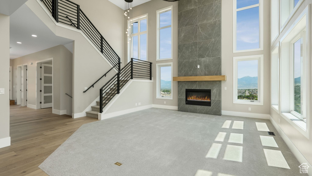 Unfurnished living room with a towering ceiling, stairway, a fireplace, wood finished floors, and recessed lighting