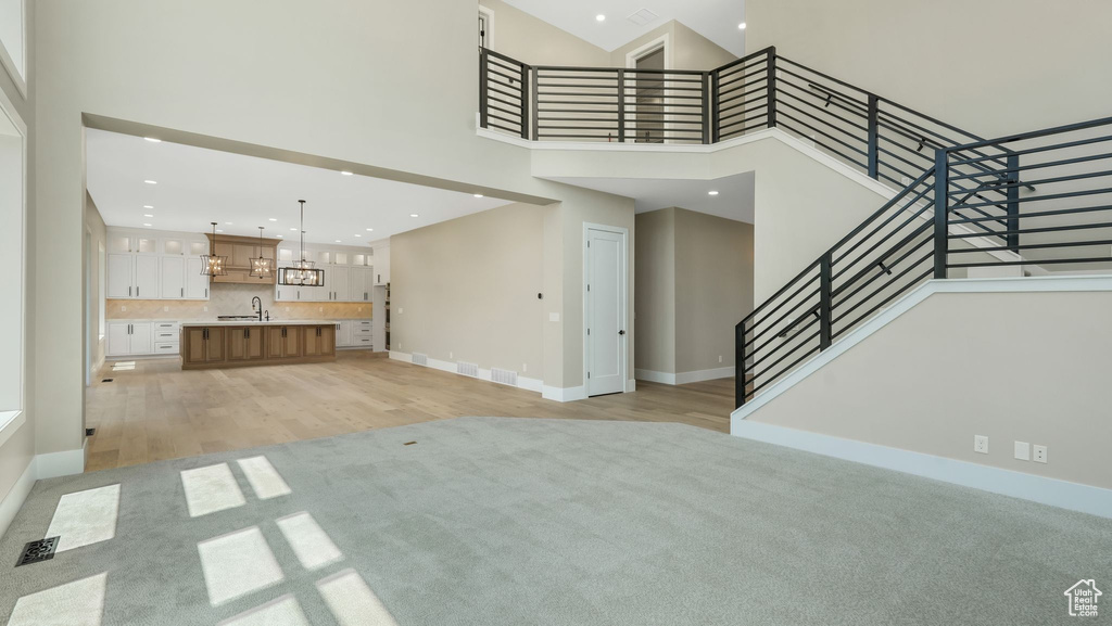 Unfurnished living room featuring a towering ceiling, a chandelier, stairs, light carpet, and recessed lighting