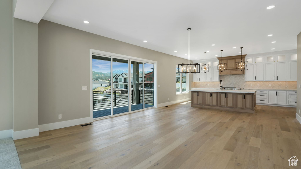 Kitchen with a chandelier, light countertops, backsplash, white cabinetry, and glass insert cabinets