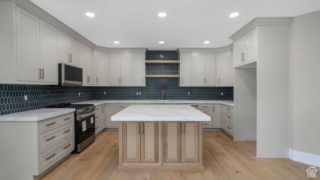 Kitchen featuring stainless steel appliances, open shelves, decorative backsplash, a kitchen island, and light wood-style floors