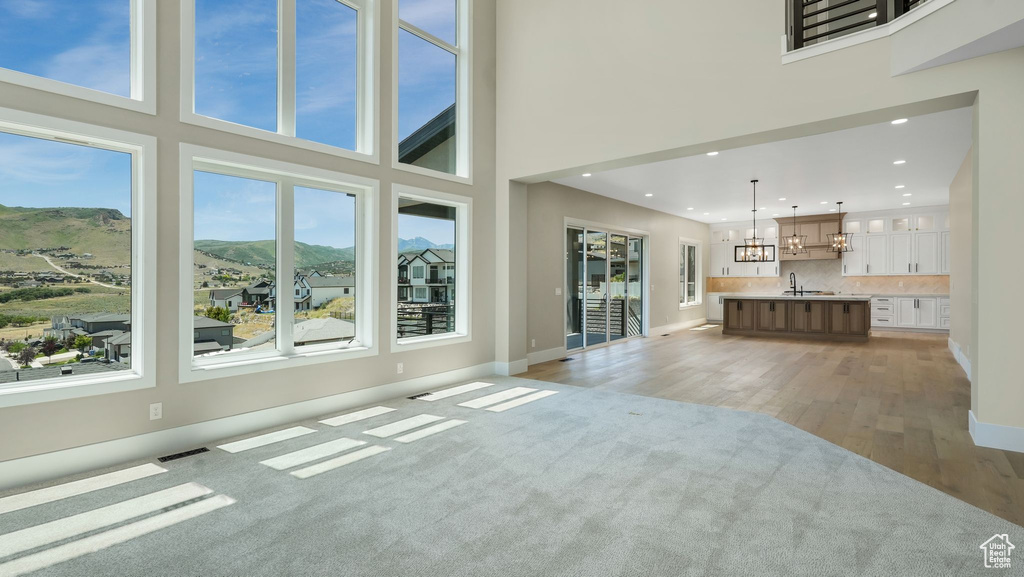 Unfurnished living room featuring a chandelier, a mountain view, light wood-style floors, a towering ceiling, and recessed lighting