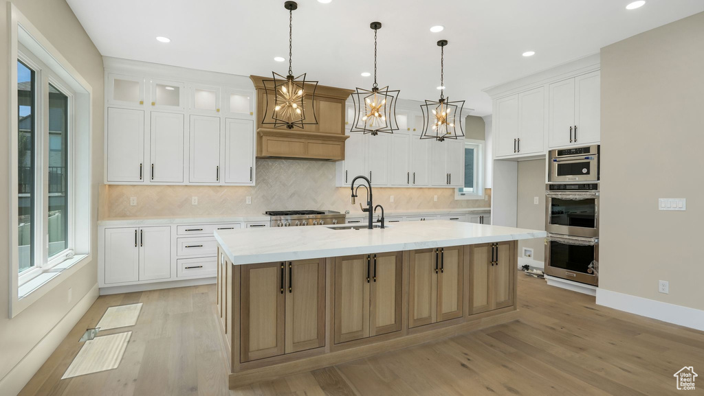 Kitchen featuring light wood finished floors, a chandelier, backsplash, a center island with sink, and recessed lighting