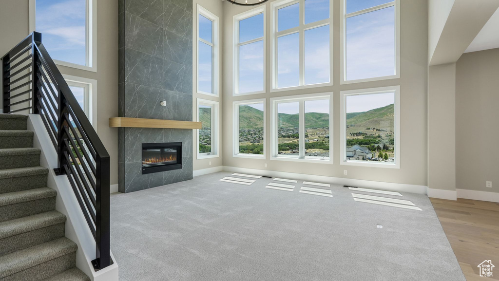 Unfurnished living room with a high ceiling, a mountain view, a tile fireplace, stairway, and carpet flooring
