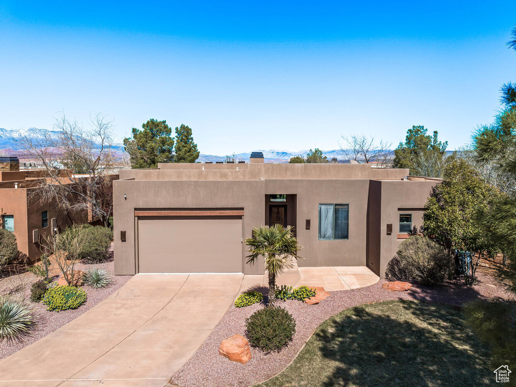 Pueblo revival-style home with driveway, an attached garage, stucco siding, and a mountain view