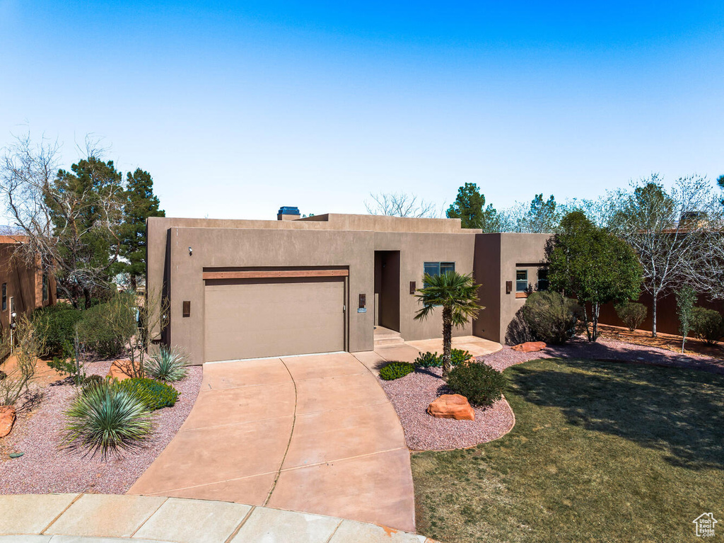 Pueblo-style home featuring a garage, stucco siding, driveway, and a front yard