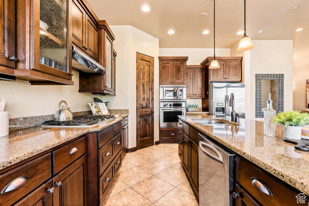 Kitchen with appliances with stainless steel finishes, under cabinet range hood, pendant lighting, light stone counters, and recessed lighting