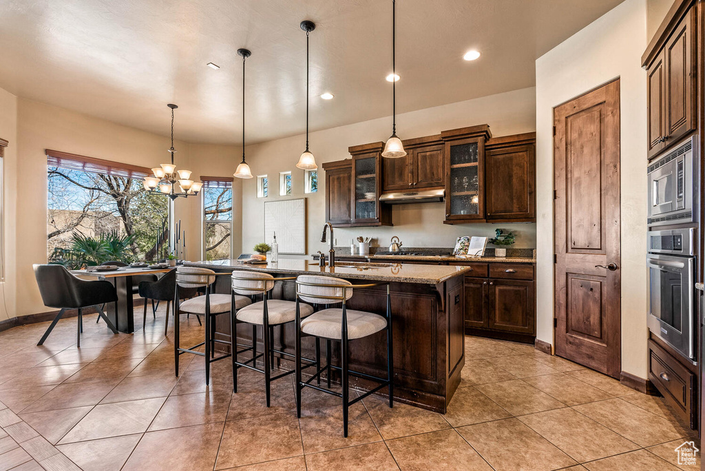 Kitchen featuring appliances with stainless steel finishes, under cabinet range hood, a breakfast bar area, a center island with sink, and recessed lighting