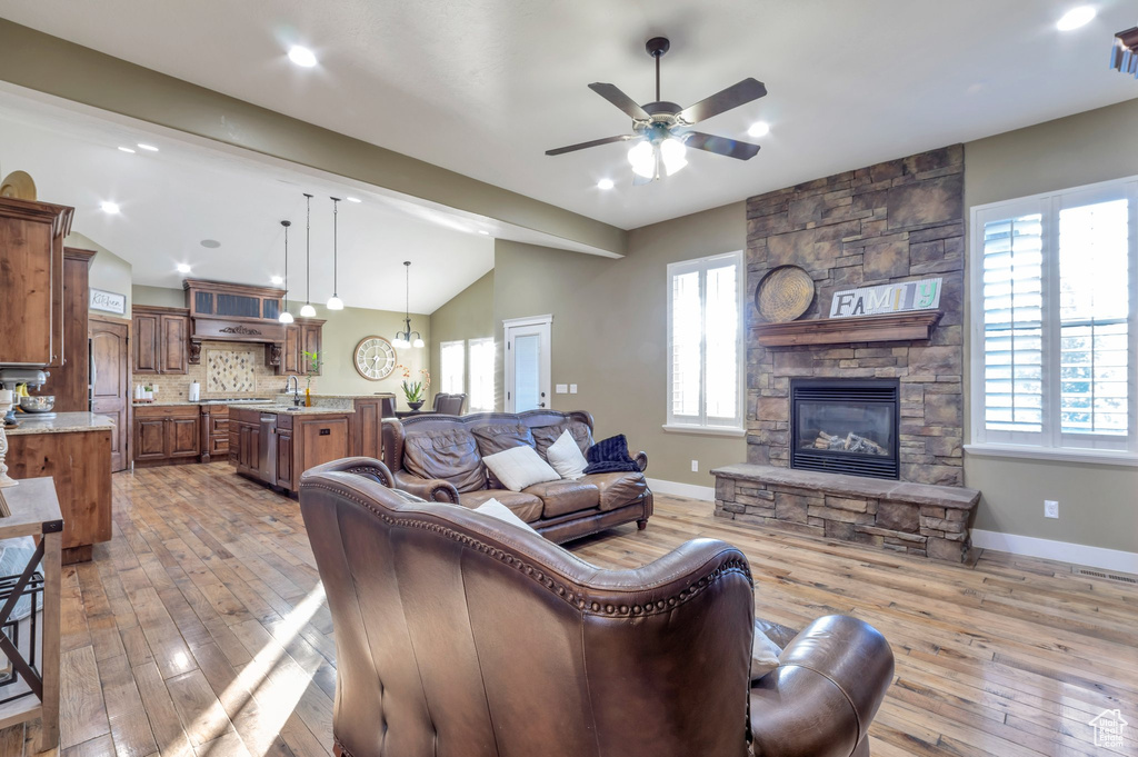 Living area with vaulted ceiling, a ceiling fan, a fireplace, light wood finished floors, and plenty of natural light