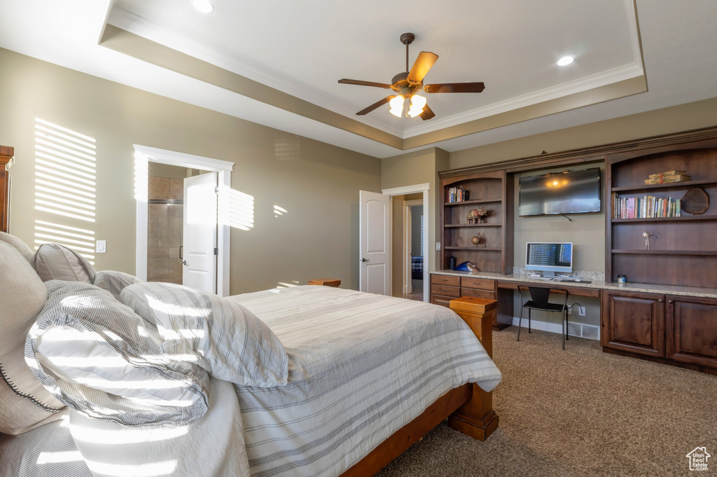 Bedroom featuring a raised ceiling, built in desk, ornamental molding, and light colored carpet
