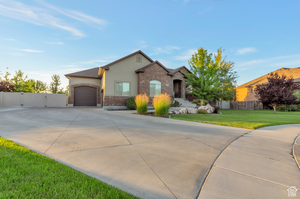 View of front facade with driveway, a garage, stucco siding, a gate, and brick siding