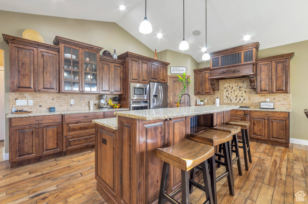 Kitchen with stainless steel appliances, lofted ceiling, light wood-type flooring, tasteful backsplash, and glass insert cabinets