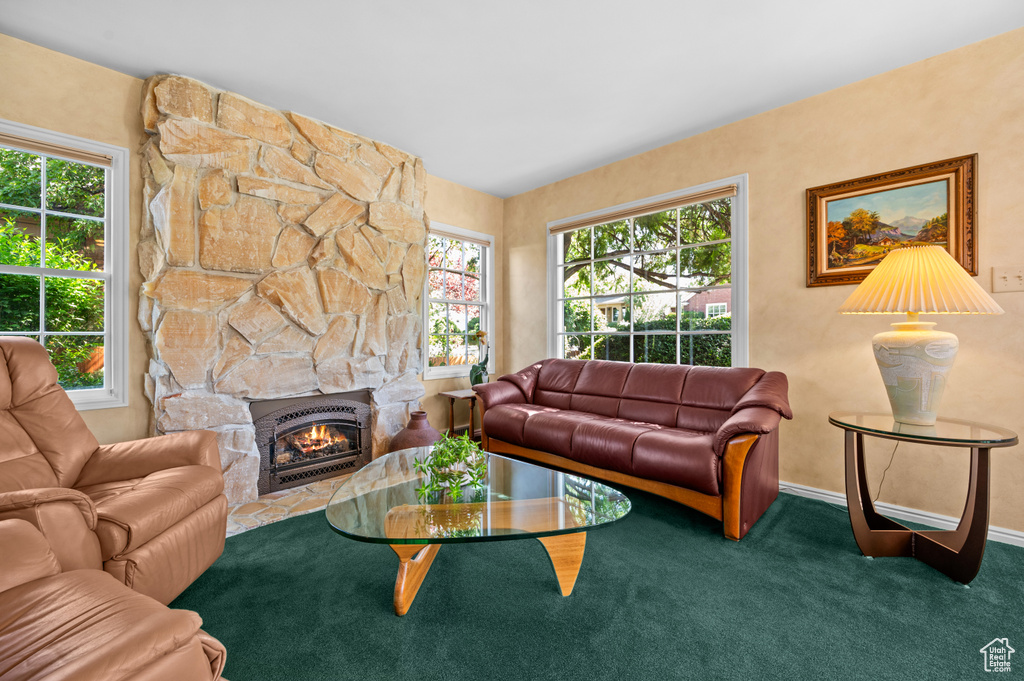 Carpeted living area featuring a stone fireplace and baseboards