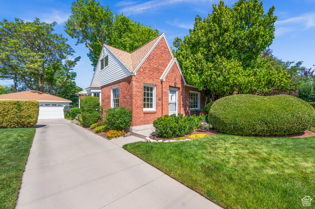 View of front of property featuring brick siding, a garage, an outdoor structure, and a front lawn