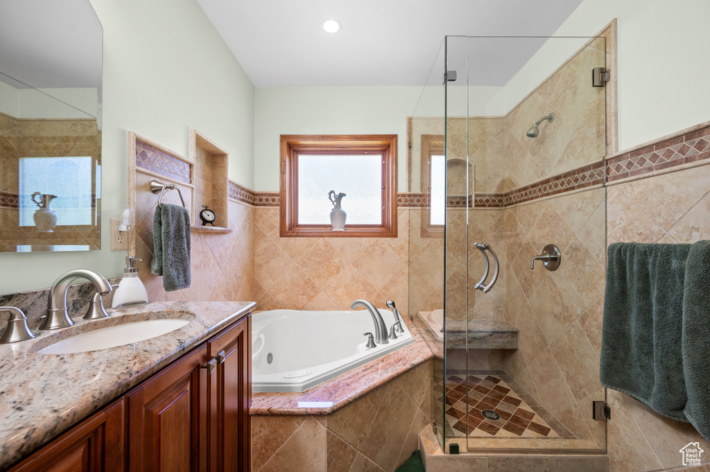 Bathroom featuring a jetted tub, a stall shower, vanity, and tile walls