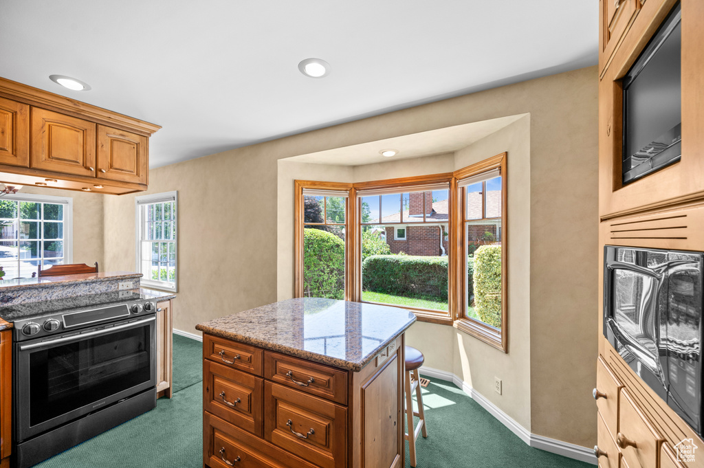 Kitchen with electric range, dark colored carpet, light stone countertops, brown cabinets, and recessed lighting