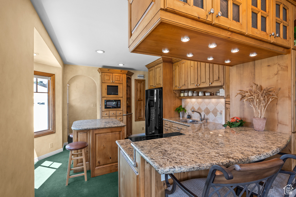 Kitchen with black appliances, a breakfast bar, light stone counters, a peninsula, and backsplash