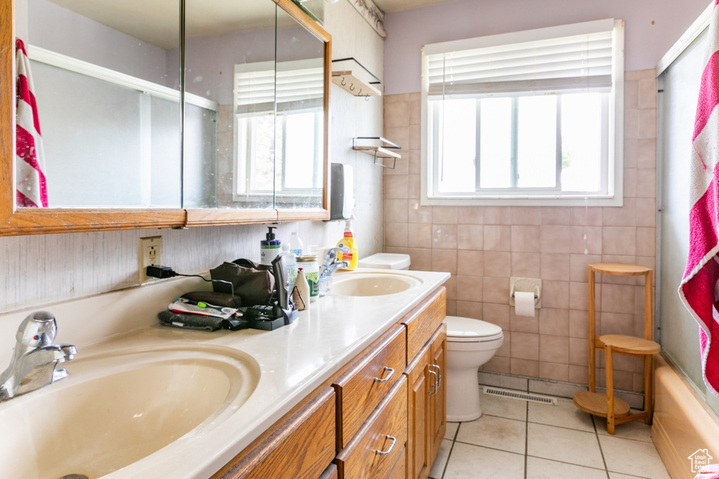 Bathroom featuring tile patterned flooring, double vanity, enclosed tub / shower combo, and tile walls
