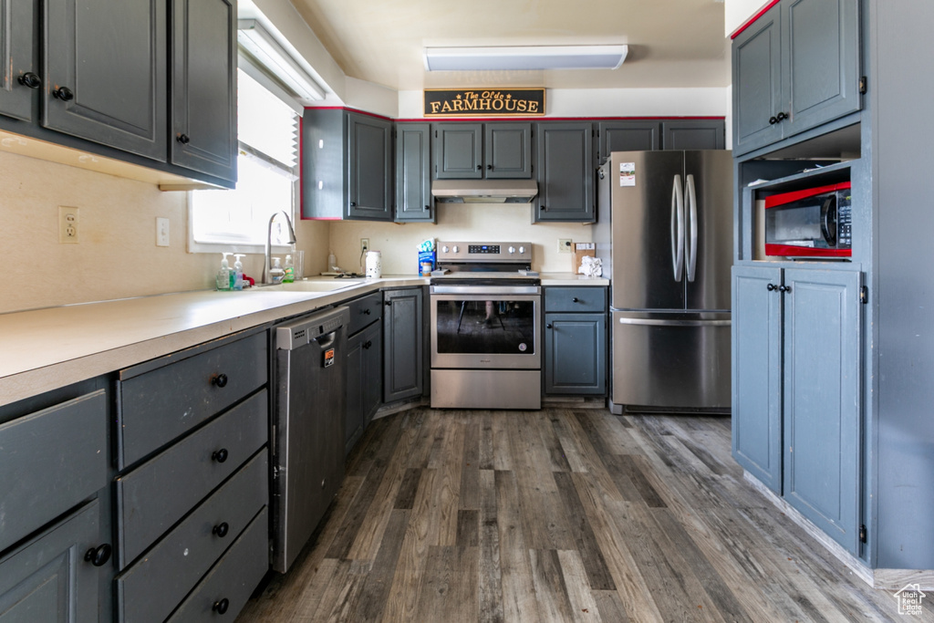 Kitchen featuring stainless steel appliances, under cabinet range hood, dark wood-style floors, and light countertops