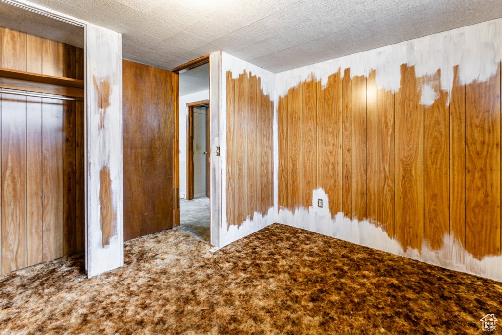 Unfurnished bedroom with carpet floors, wood walls, and a closet