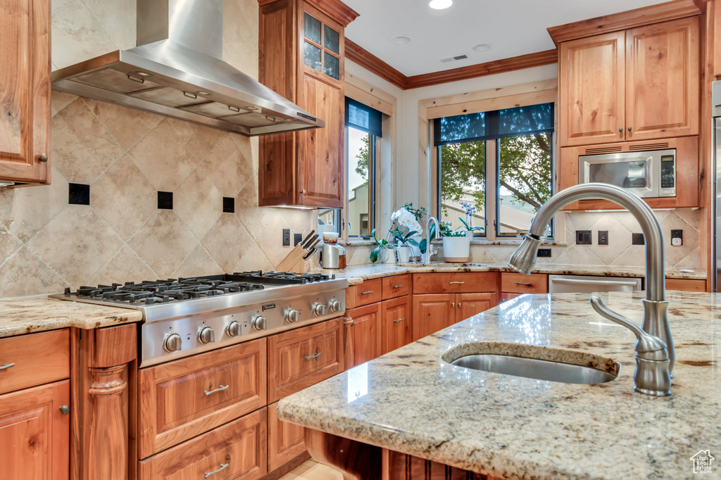 Kitchen featuring wall chimney range hood, appliances with stainless steel finishes, decorative backsplash, ornamental molding, and light stone counters