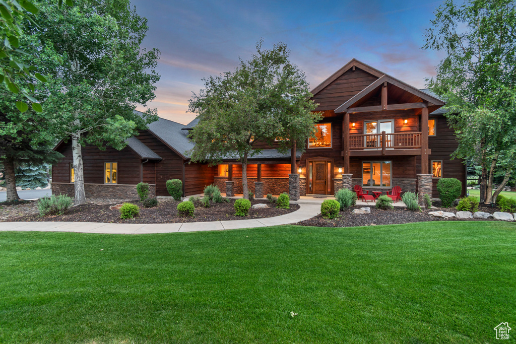 View of front facade with stone siding, covered porch, a front yard, and a balcony