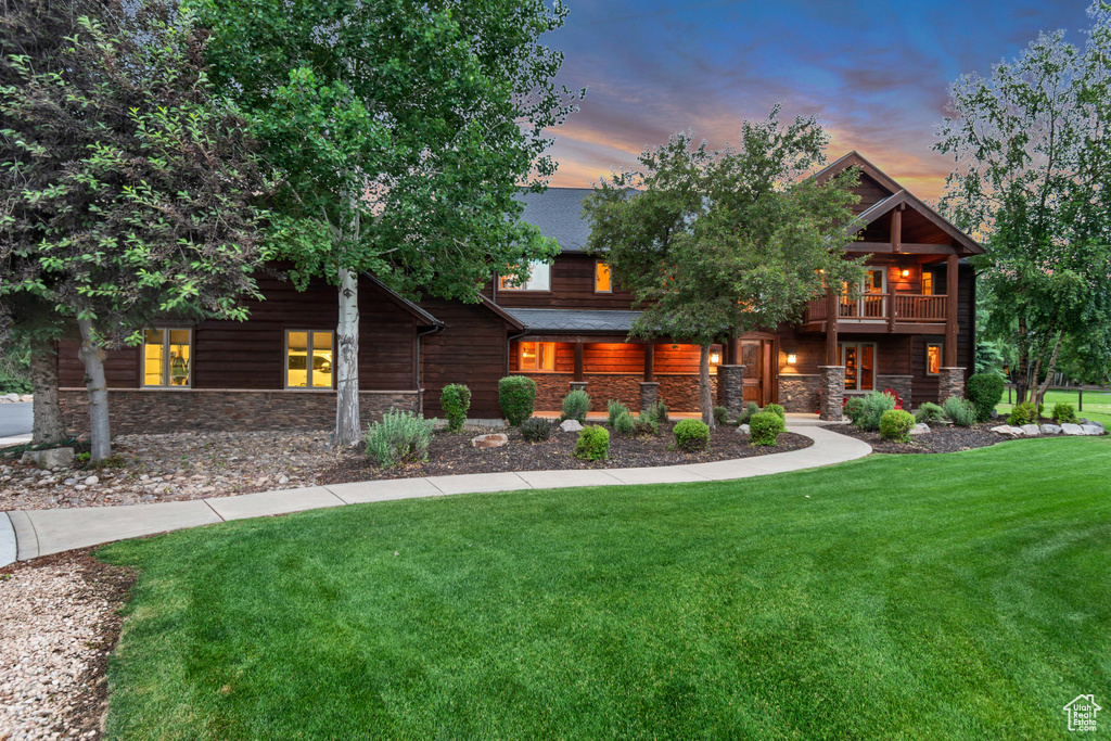 View of front of property featuring stone siding, a yard, and a balcony