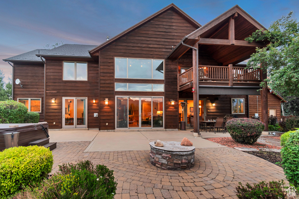 Back of property featuring a hot tub, a fire pit, a patio area, and a balcony