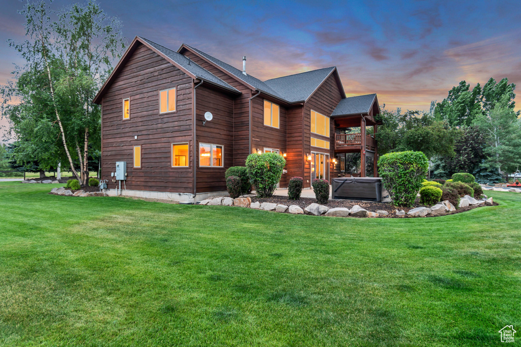 View of side of property featuring a yard, a hot tub, and a balcony