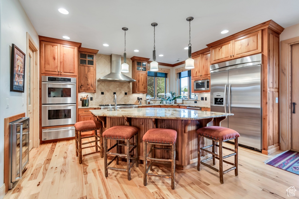 Kitchen featuring built in appliances, wall chimney range hood, a warming drawer, beverage cooler, and light wood-type flooring