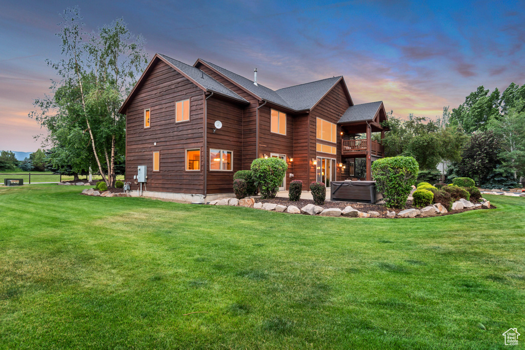 Back of property at dusk with a balcony, a yard, and a hot tub