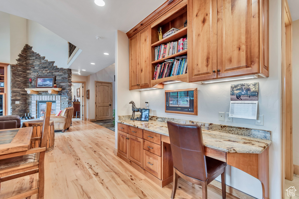 Kitchen with light wood finished floors, light stone countertops, open shelves, a stone fireplace, and recessed lighting