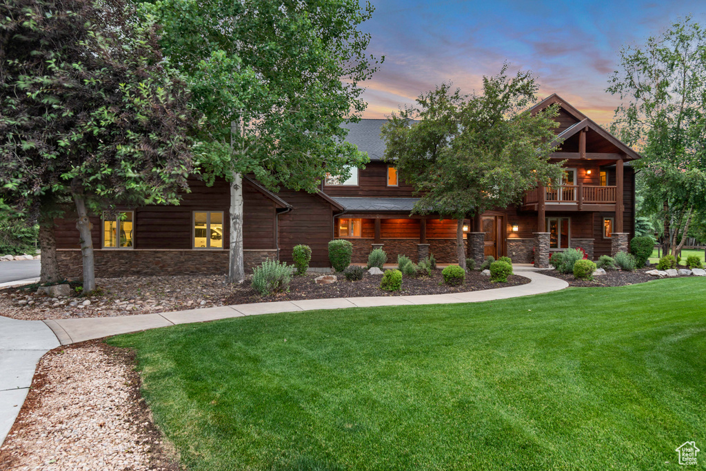 View of front of house with stone siding, a lawn, a balcony, and a shingled roof