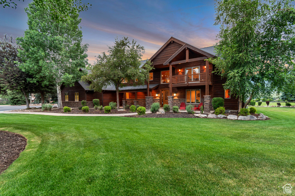 View of front of property with a balcony, a front lawn, and stone siding
