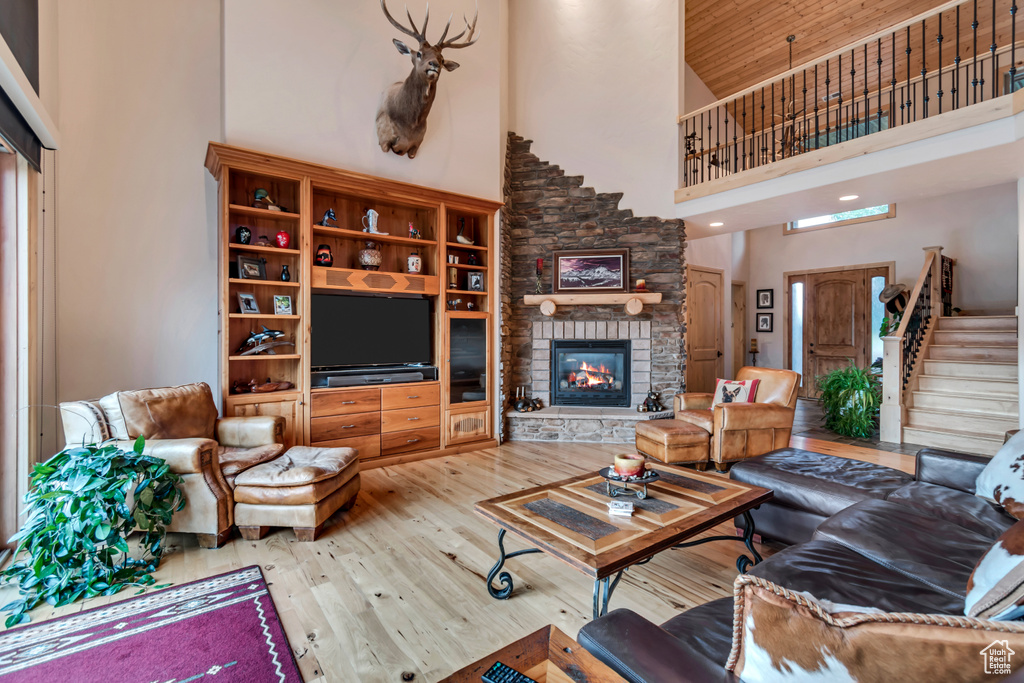 Living area featuring high vaulted ceiling, hardwood / wood-style flooring, a fireplace, stairs, and wooden ceiling